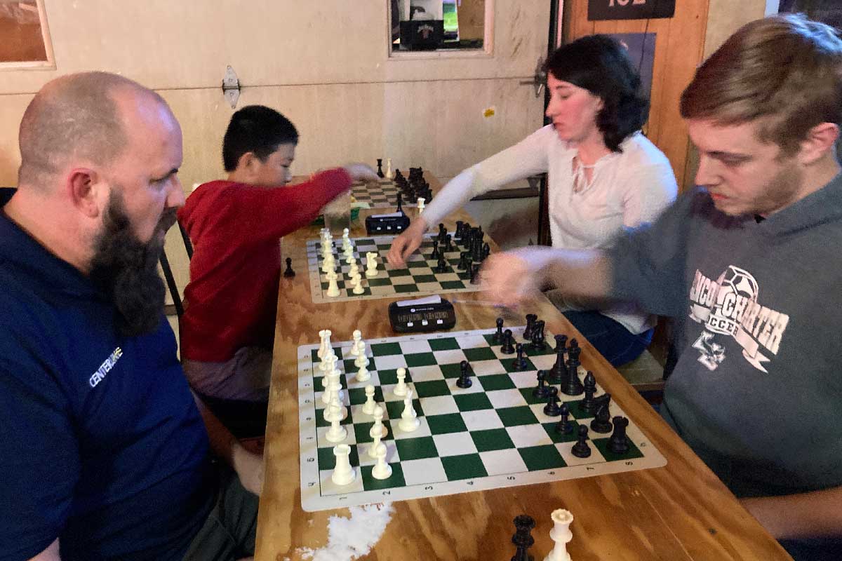 Young boy and a young lady playing chess with two gentlemen